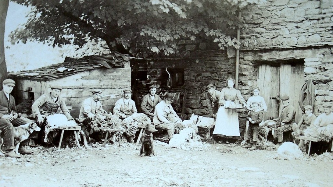 Historisk sort-hvidt fotografi af landarbejdere i traditionelt arbejdstøj fra starten af det 20. århundrede.